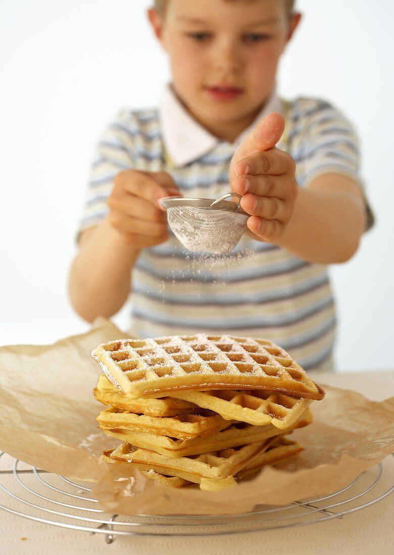 Junge streut Puderzucker über einen Stapel Waffeln