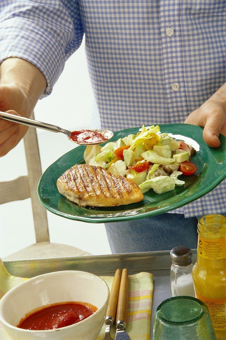 Mann gibt Ketchup zu gegrilltem Putenschnitzel mit Salat