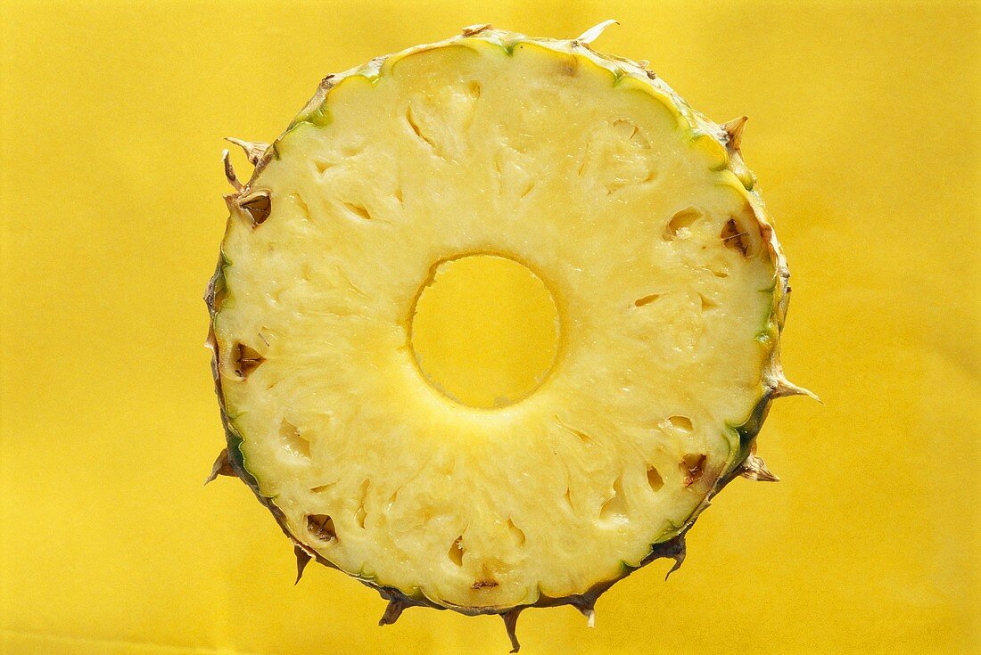Eine Ananasscheibe vor gelbem Hintergrund