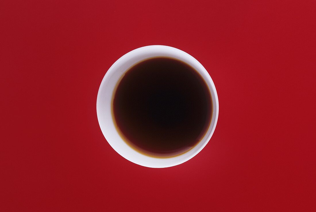 Soy sauce in a small white bowl on red background