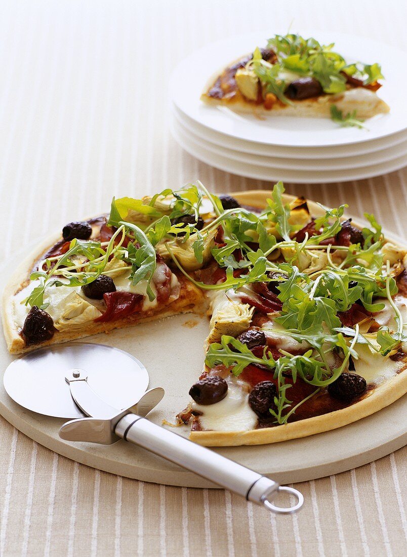 Pizza with olives, artichokes and rocket with pizza cutter