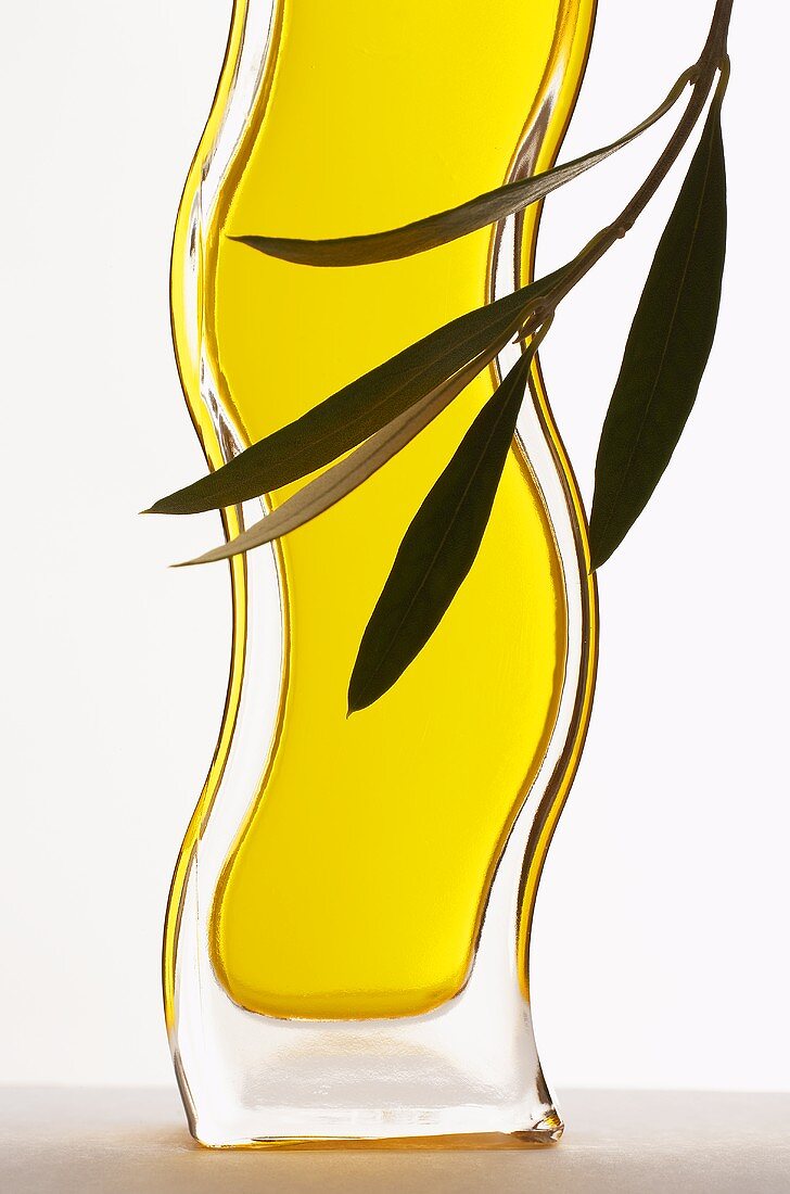 Eine geschwungene Flasche Olivenöl mit Olivenblättern