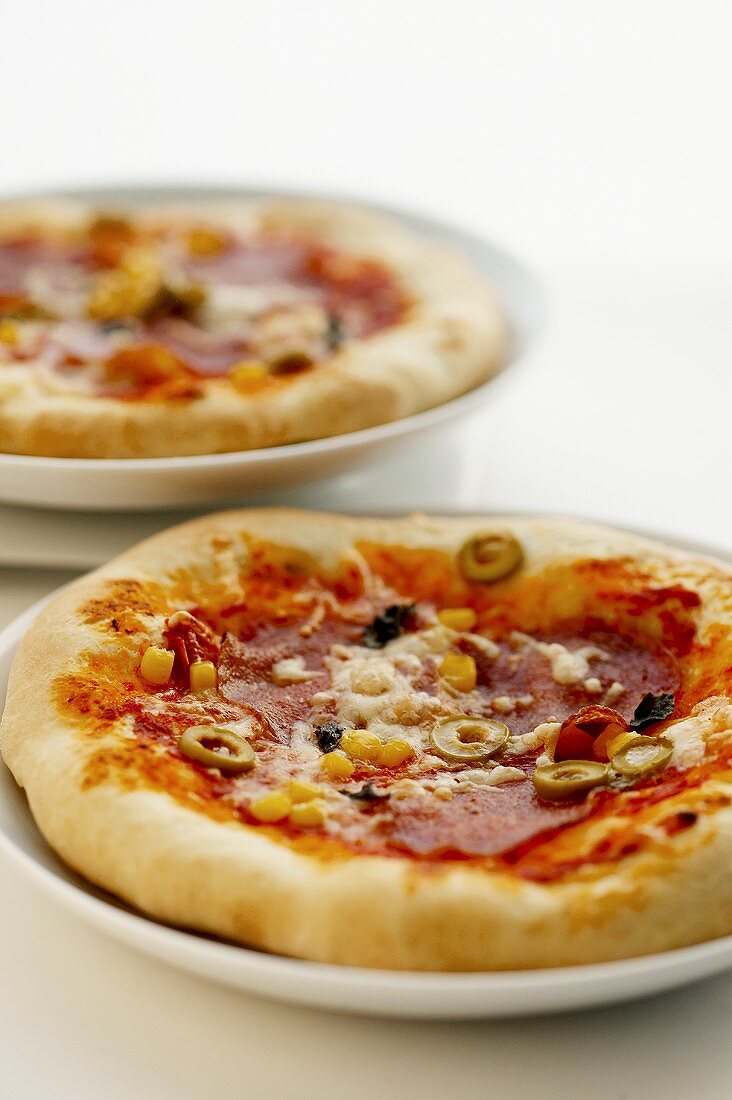 Two salami pizzas with sliced olives and sweetcorn