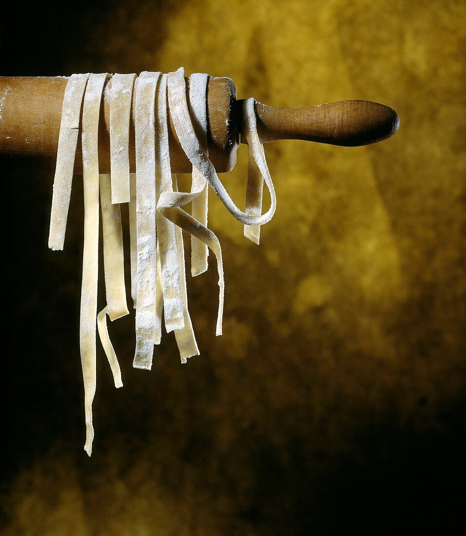 Home-made ribbon pasta hanging on a rolling pin