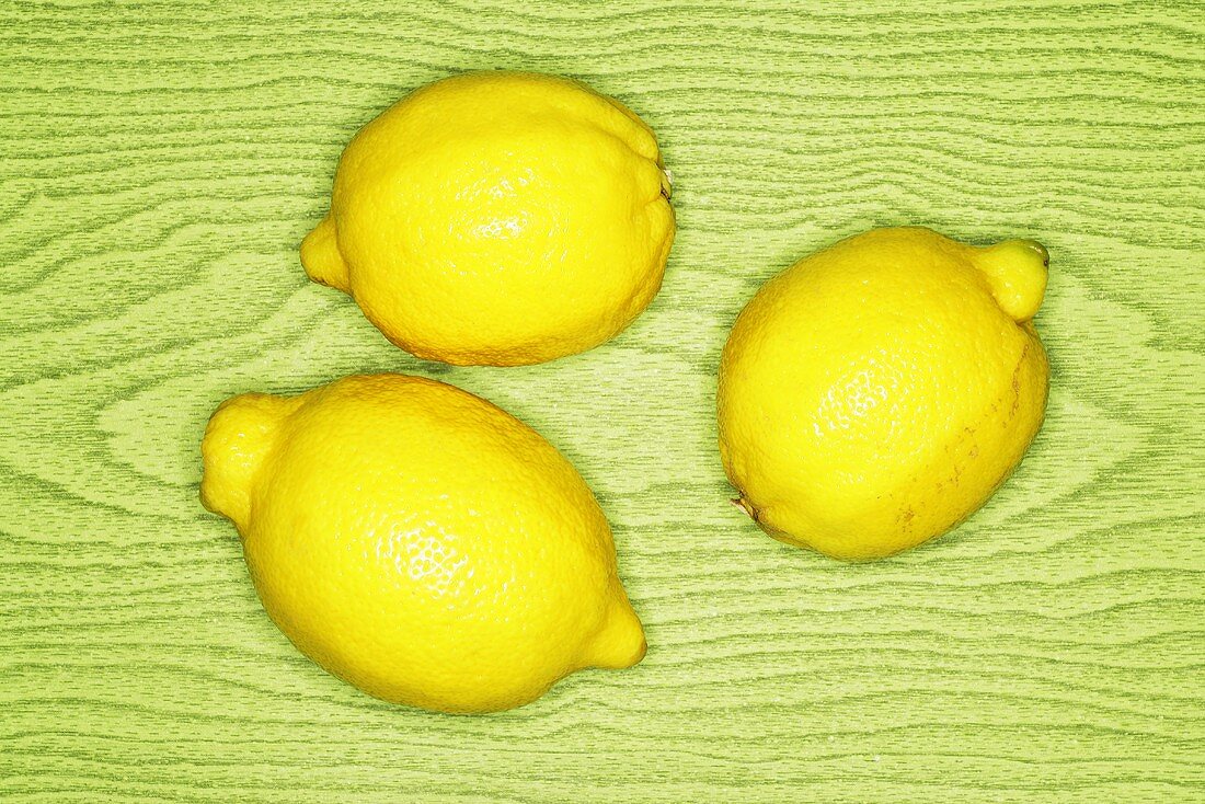 Three lemons on green wooden background