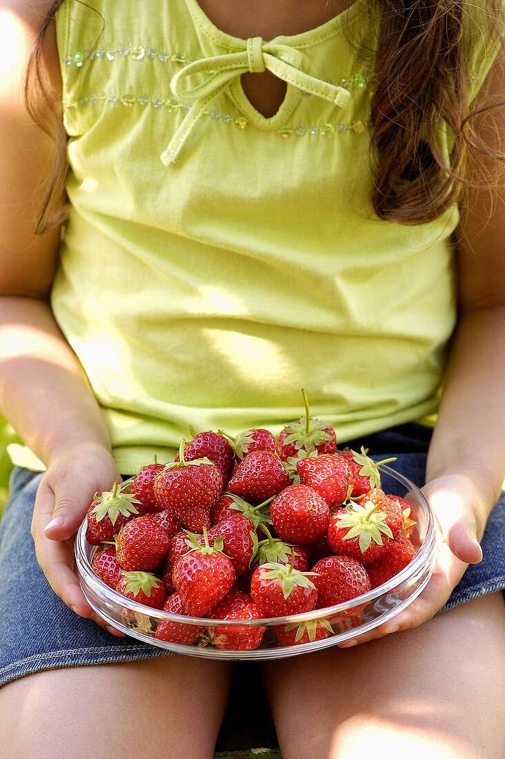 Mädchen hält Glasschüssel mit Erdbeeren