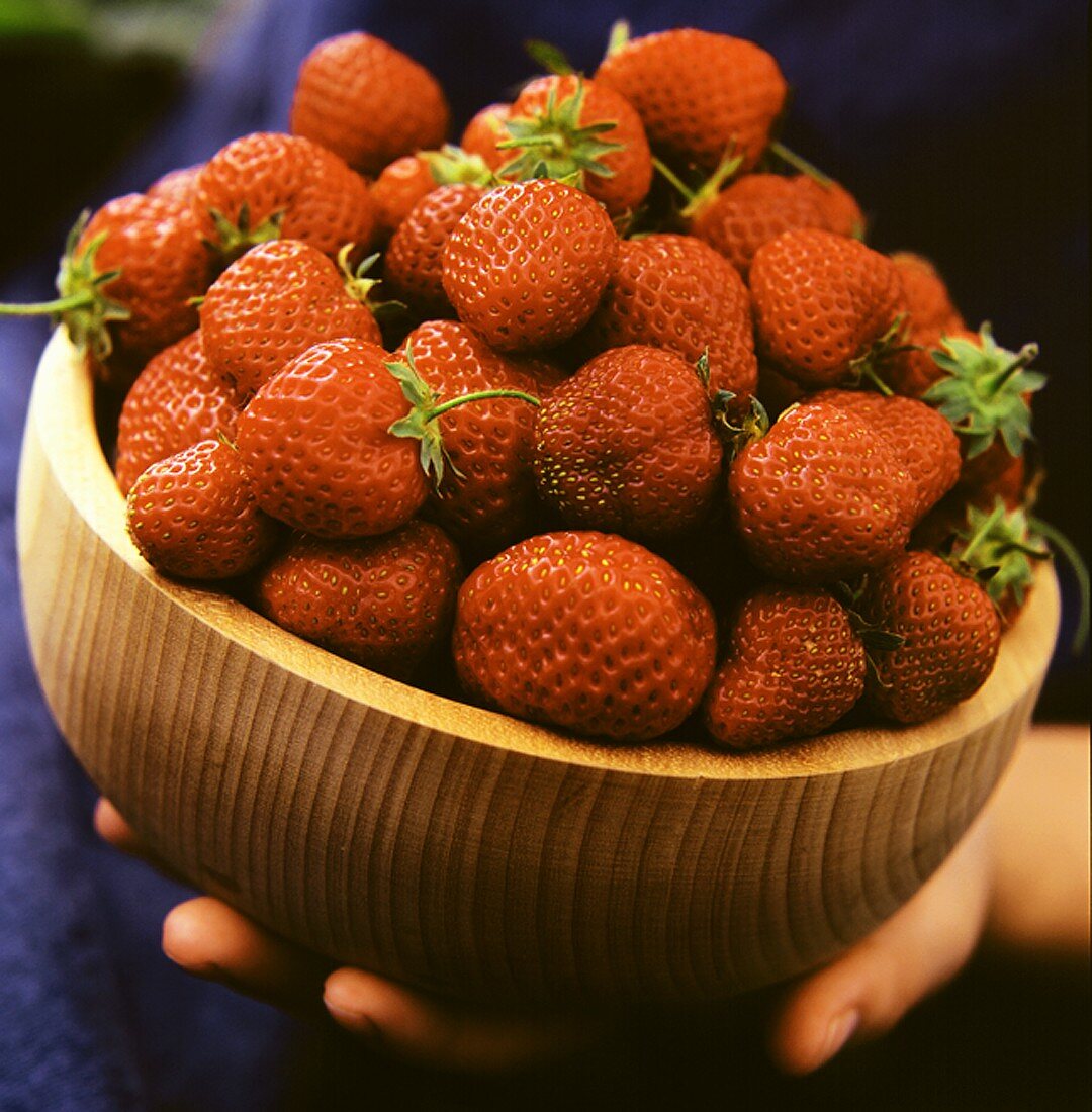 Hand hält Holzschale mit frischen Erdbeeren