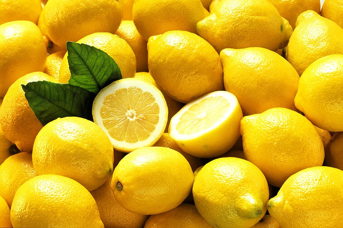 Viele ganze Zitronen und zwei Zitronenhälften (bildfüllend)