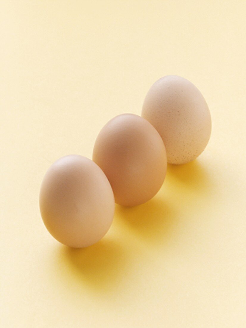 Three Brown Eggs Standing on a Yellow Background