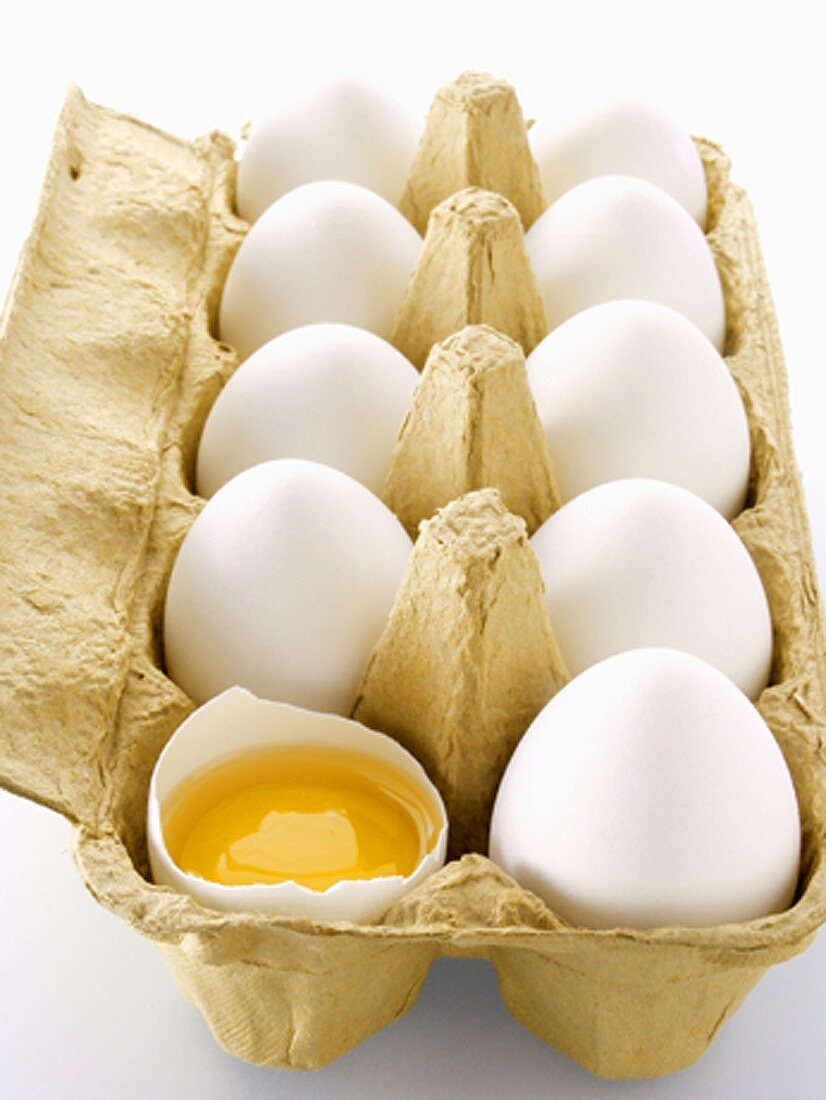 weiße Eier im Eierkarton, eines davon aufgeschlagen