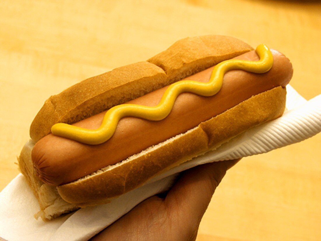 Hand hält Hot Dog mit Senf