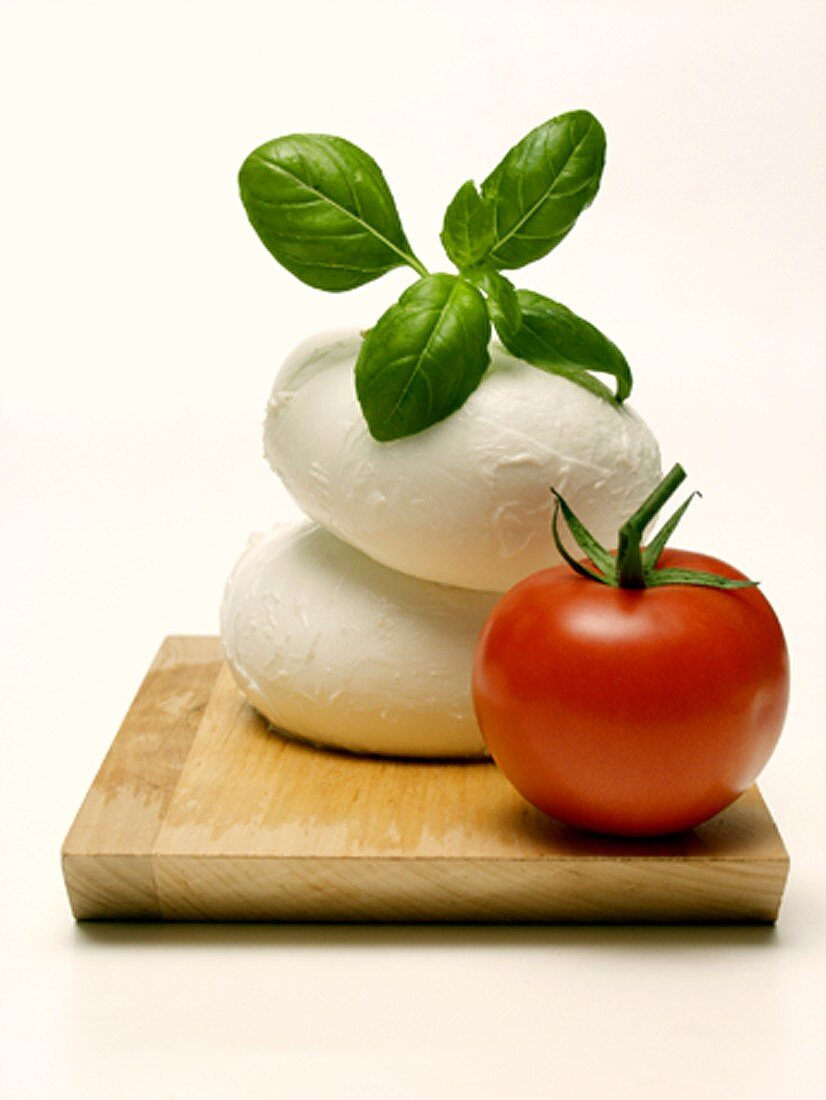 Two Mozzarella Balls with Basil and Tomato on Wooden Board