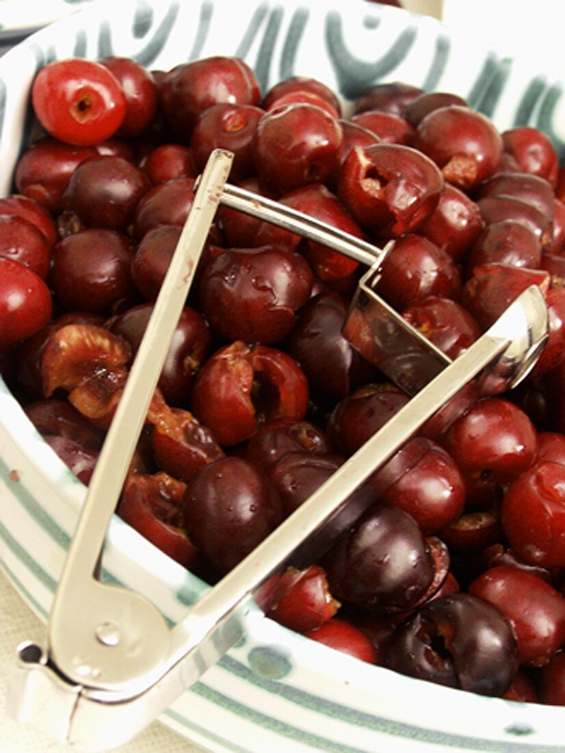 Cherry Pitter Resting on a Bowl of Pitted Cherries