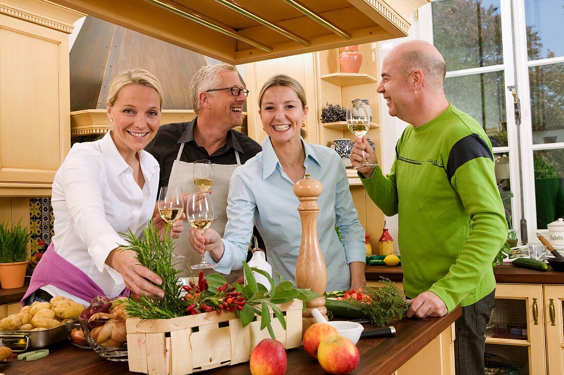 Zwei Paare mit Weissweingläsern beim Kochen