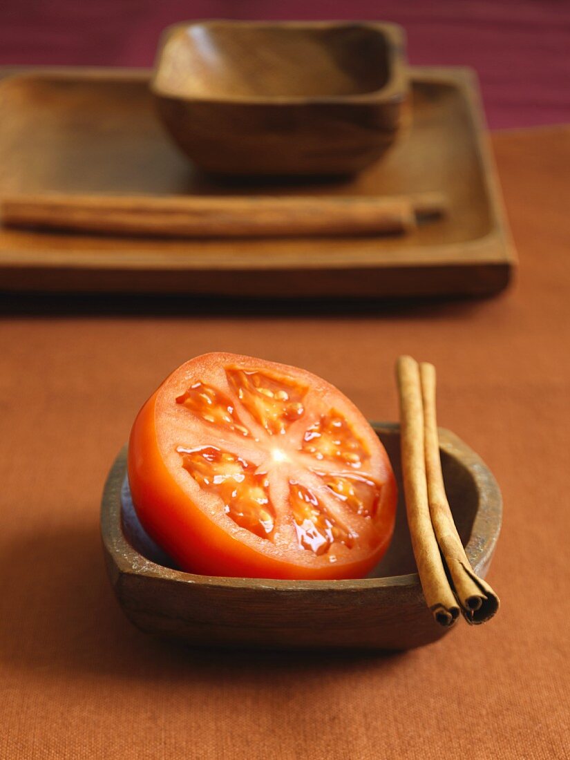 Tomatenhälfte mit Zimtstangen in Holzschale