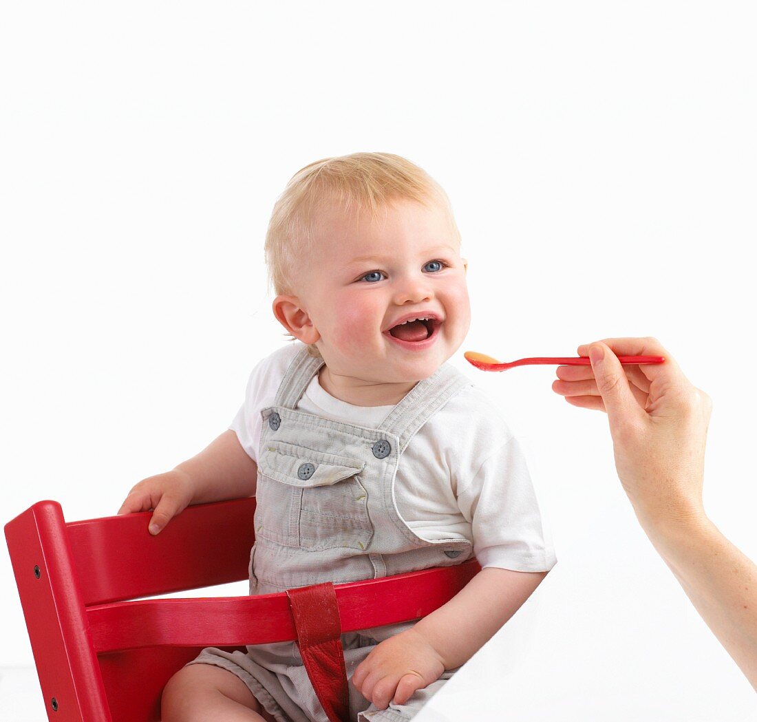 Baby sitzt im Kinderstuhl und wird gefüttert