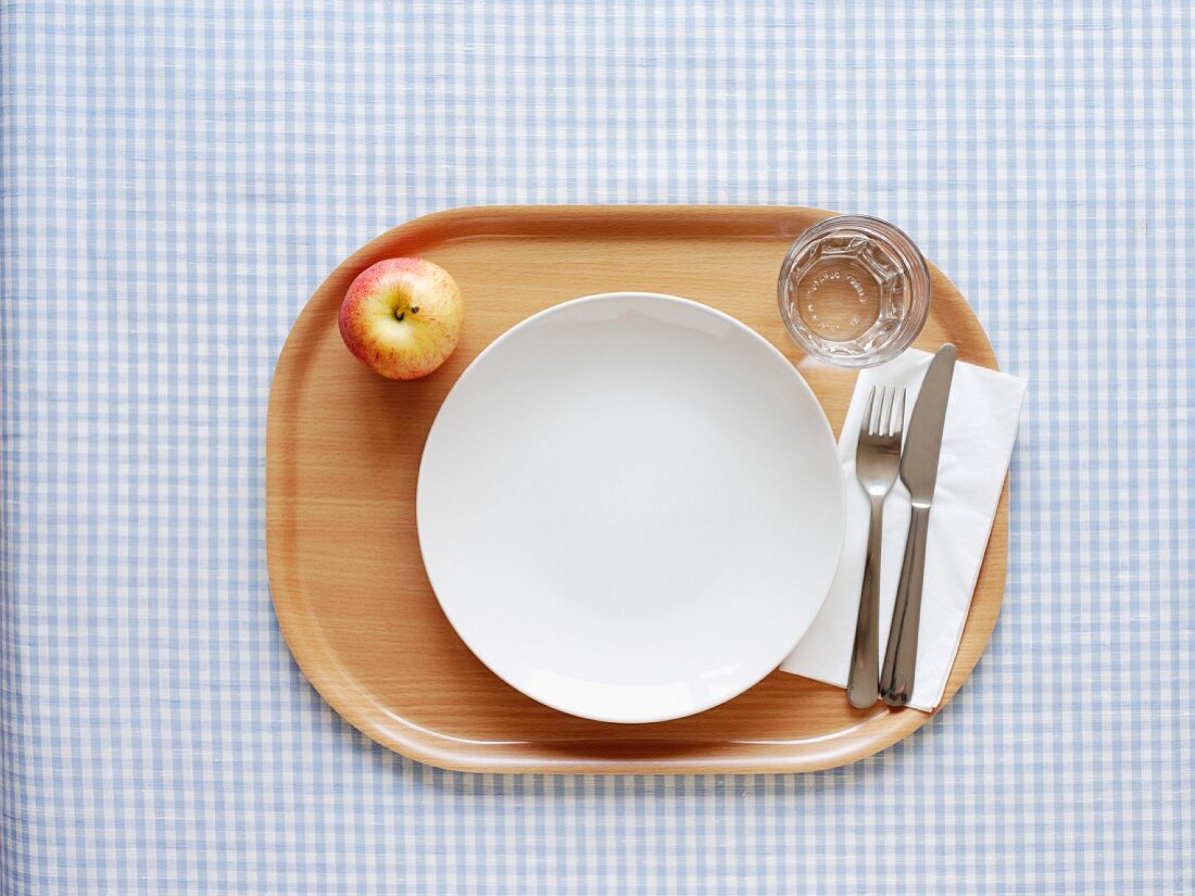 Empty plate, cutlery, glass and apple on tray
