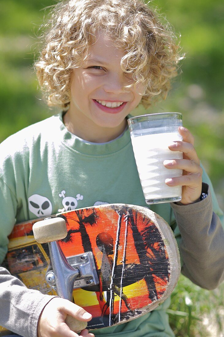 Junge mit Skateboard unter dem Armr trinkt ein Glas Milch