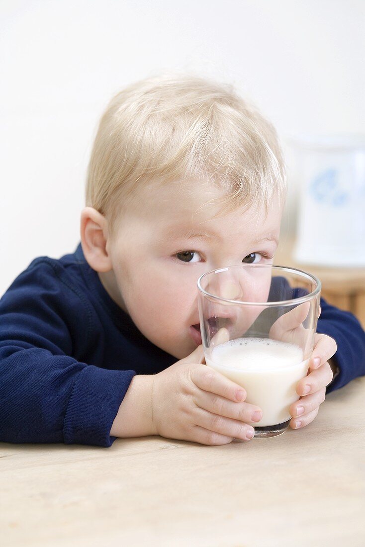 Kleiner Junge drückt seine Nase an ein Glas mit Milch