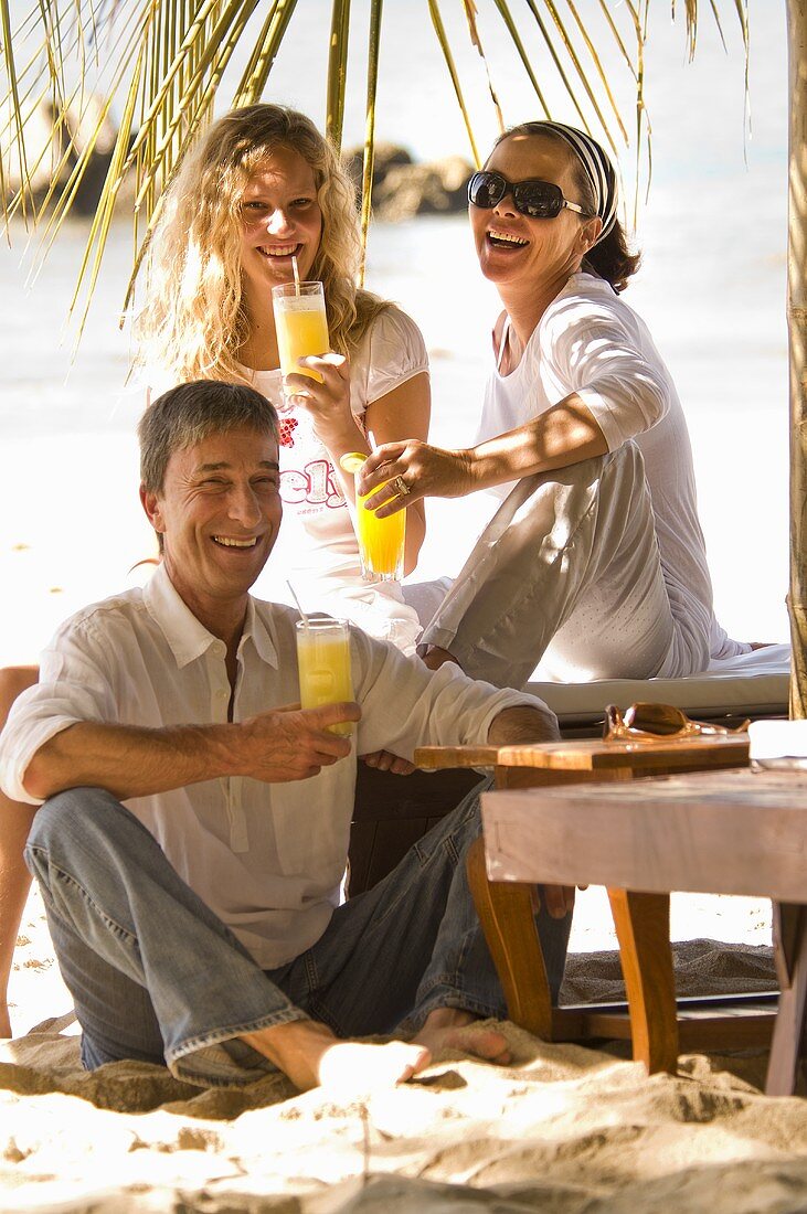 Vater, Mutter und Tochter trinken Säfte am Strand