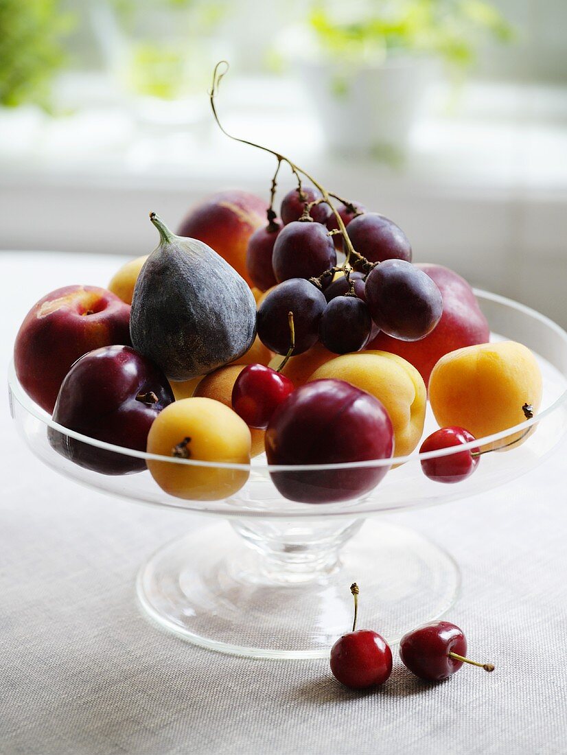 Plums, figs, grapes etc. on glass pedestal stand
