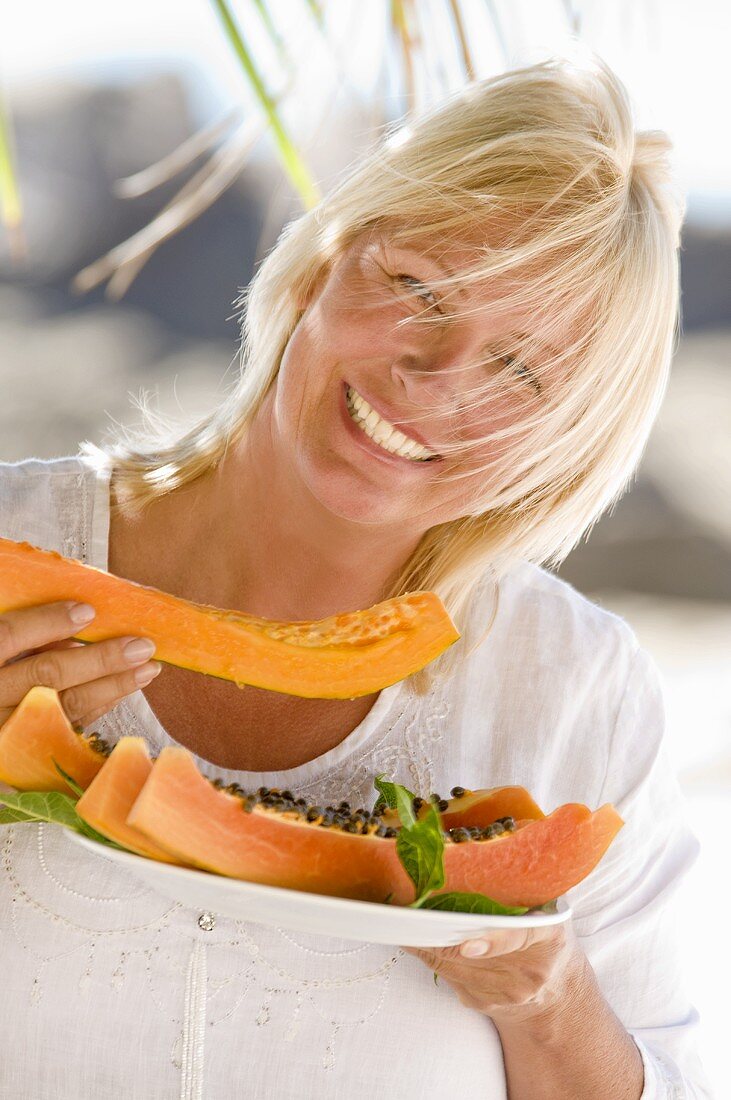 Blond woman eating papaya out of doors