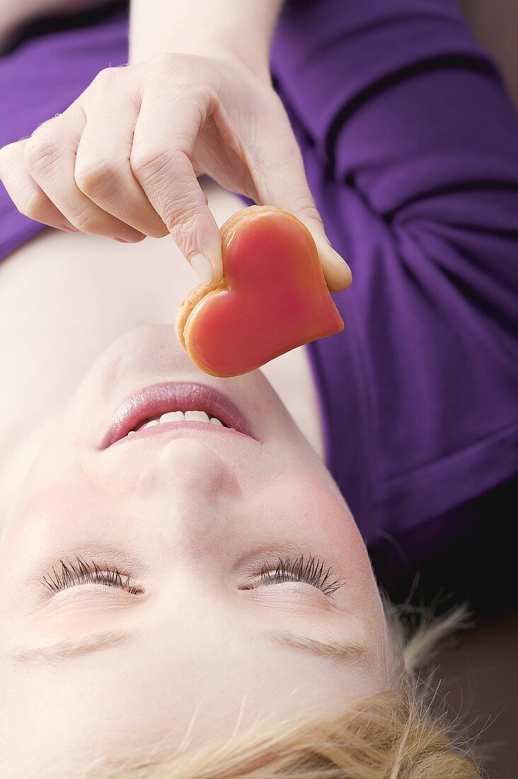 Young woman lying down eating a heart-shaped biscuit