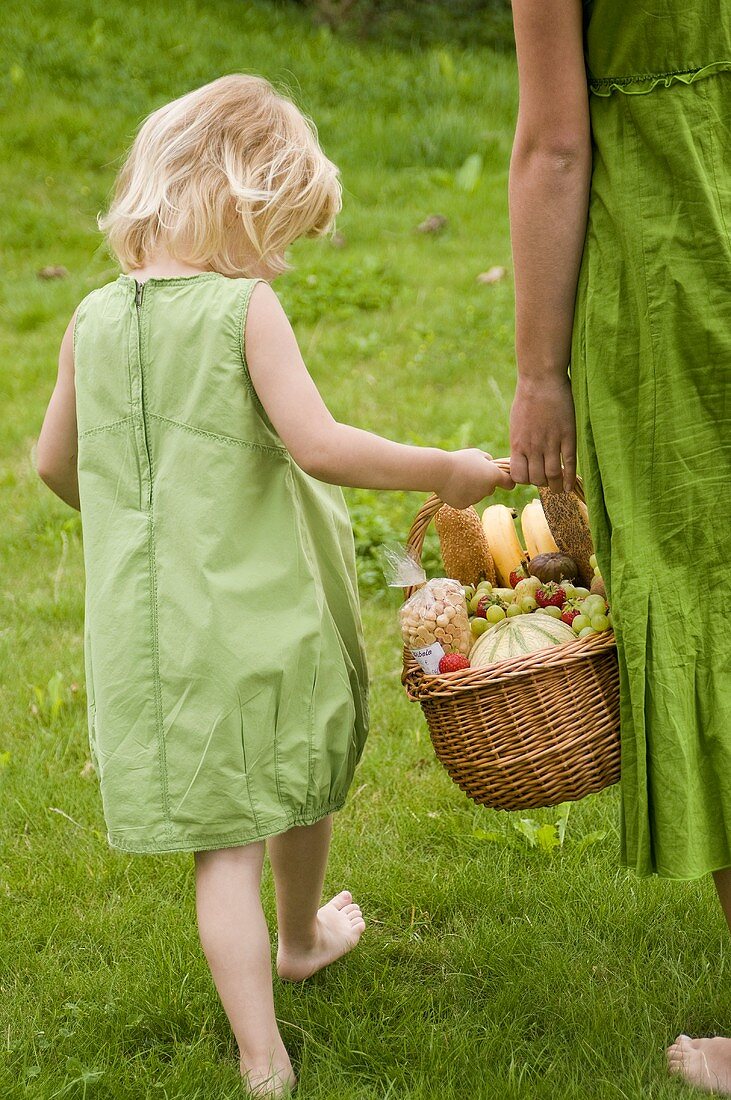 Kleines Mädchen trägt mit Mutter einen Picknickkorb