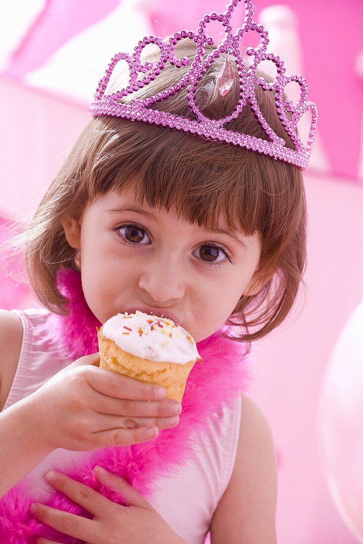 Kleines Mädchen mit Krone auf dem Kopf isst einen Muffin