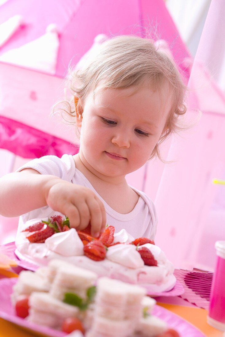 Kleines Mädchen nimmt Erdbeere von Pavlova