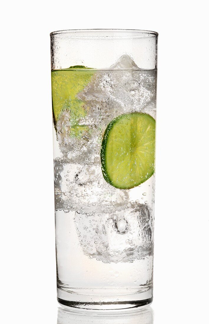 A glass of gin and tonic with slices of lime and ice cubes