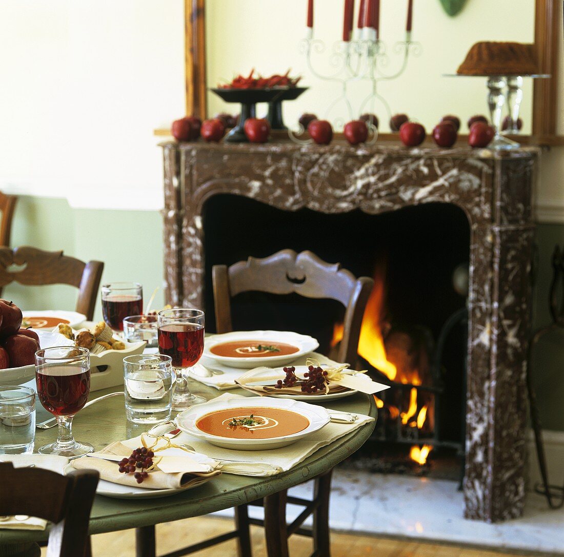 Gedeckter Tisch mit Kürbissuppe und Rotwein am Kamin