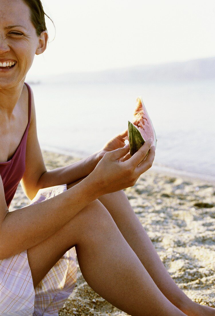 Junge Frau isst ein Stück Wassermelone am Strand