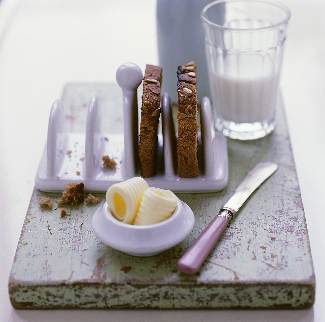 Slices of toast in toast rack, butter curls and milk