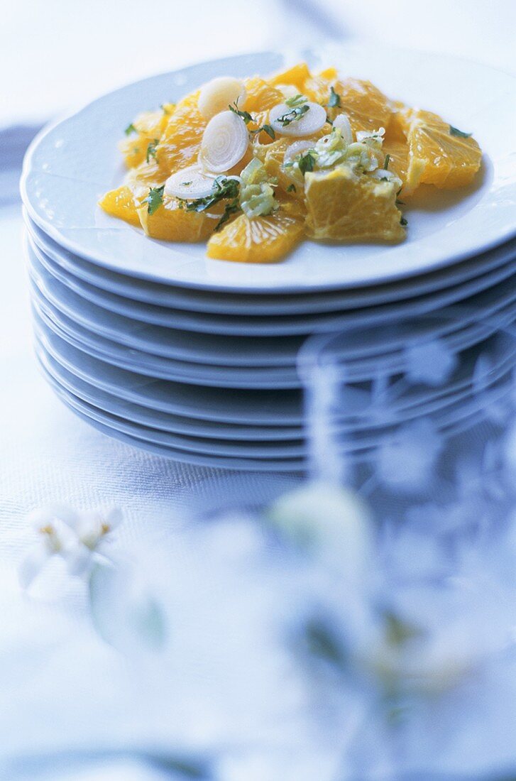 Savoury orange salad with onions on a pile of plates