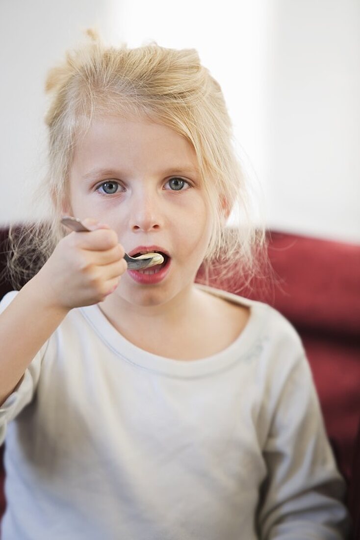 A little blonde girl eating a spoonful of yoghurt