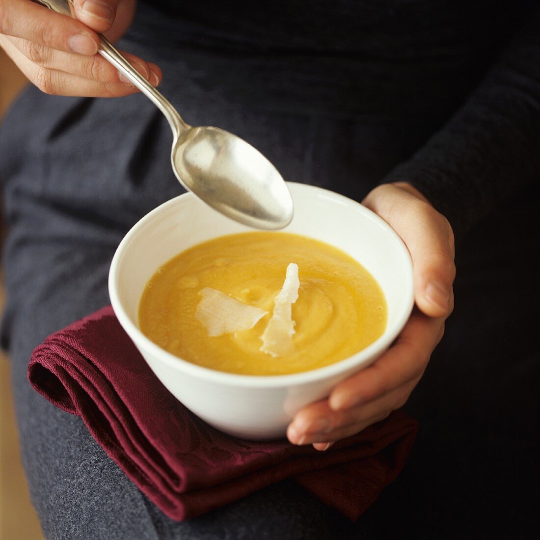 Person holding a bowl of pumpkin soup with Parmesan shavings