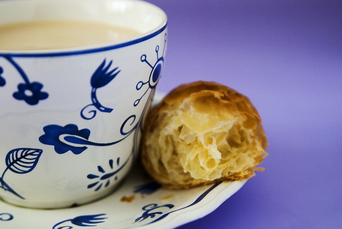 A cup of milky coffee with croissant