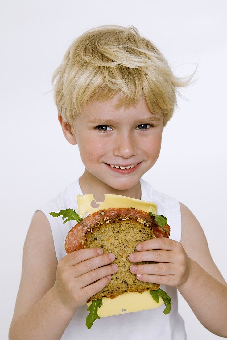 Blonder Junge hält Salami-Käse-Brot in den Händen