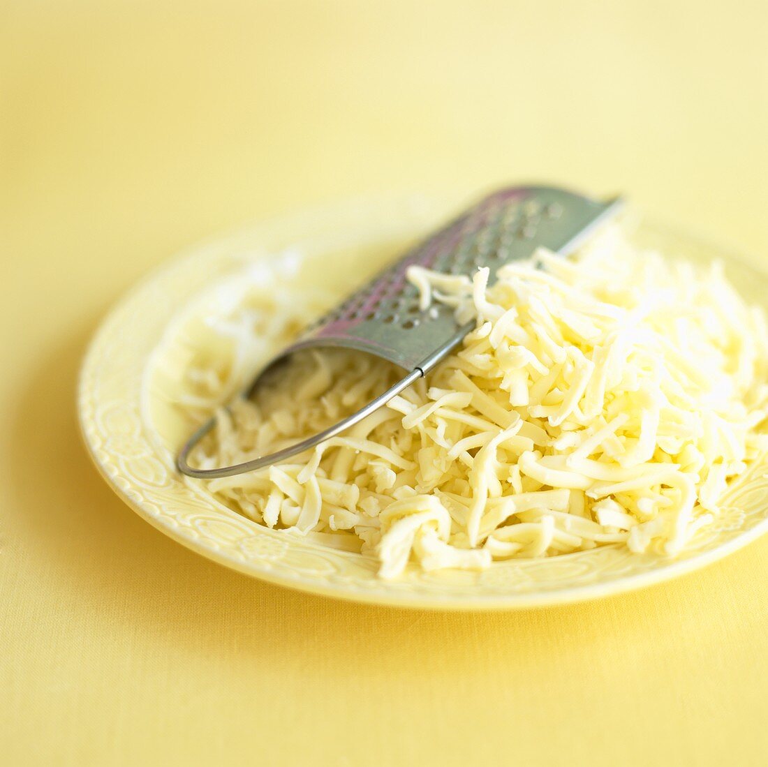 Geriebener Käse mit Reibe auf einem Teller