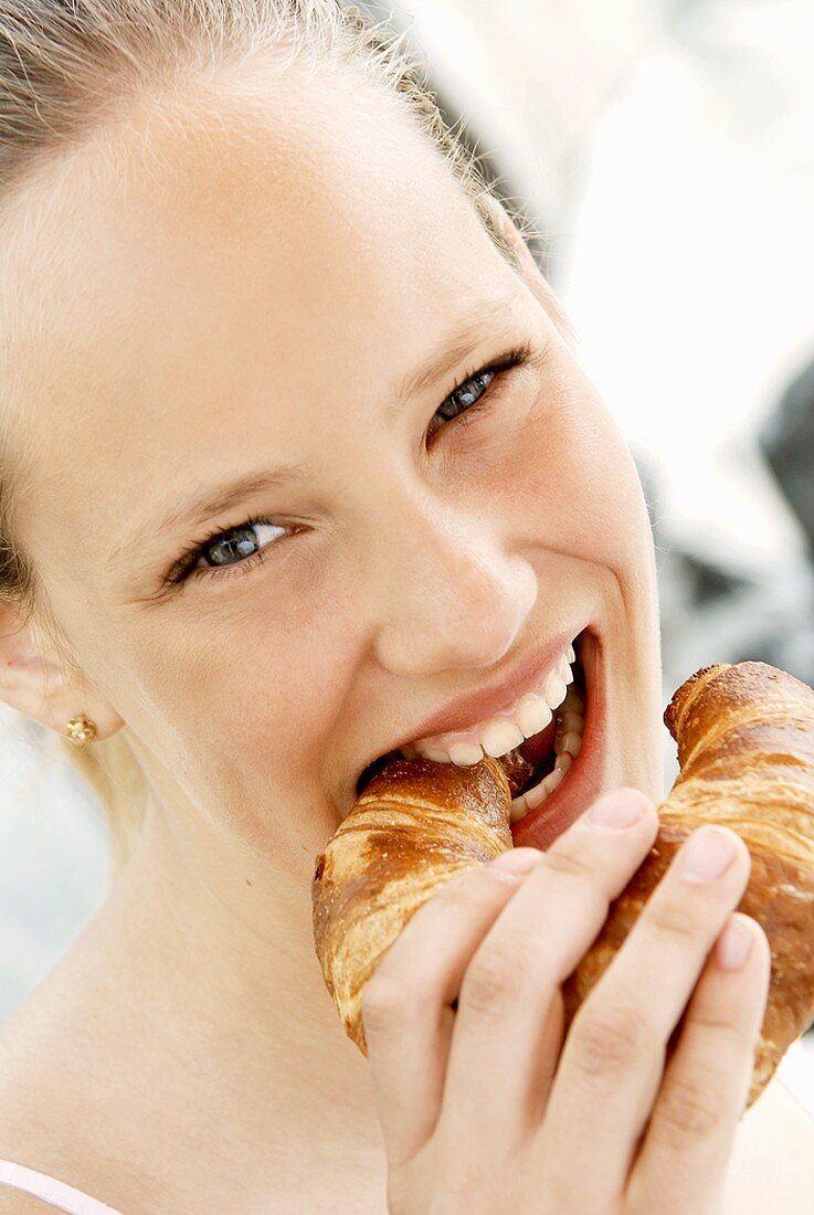 Junge Frau beisst in ein Laugen-Croissant