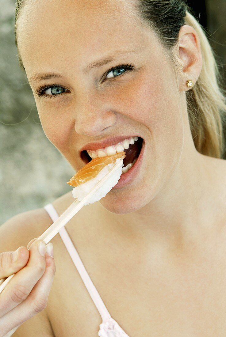 Young woman eating sushi with chopsticks