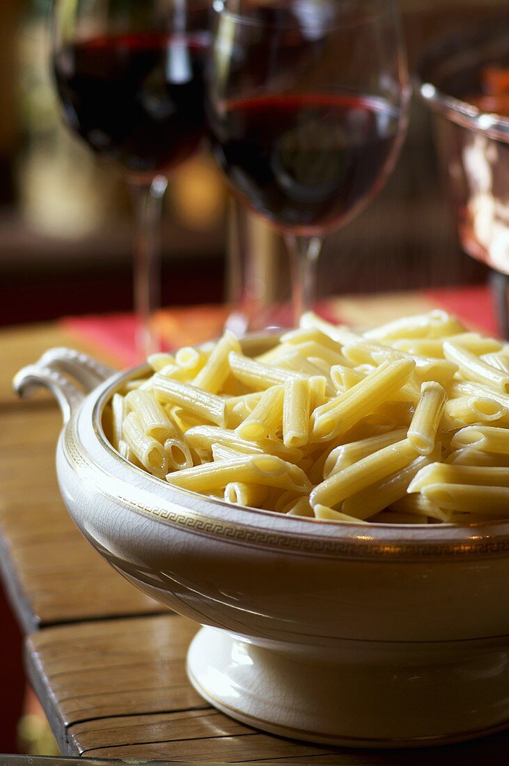Cooked pasta in a dish, glasses of red wine