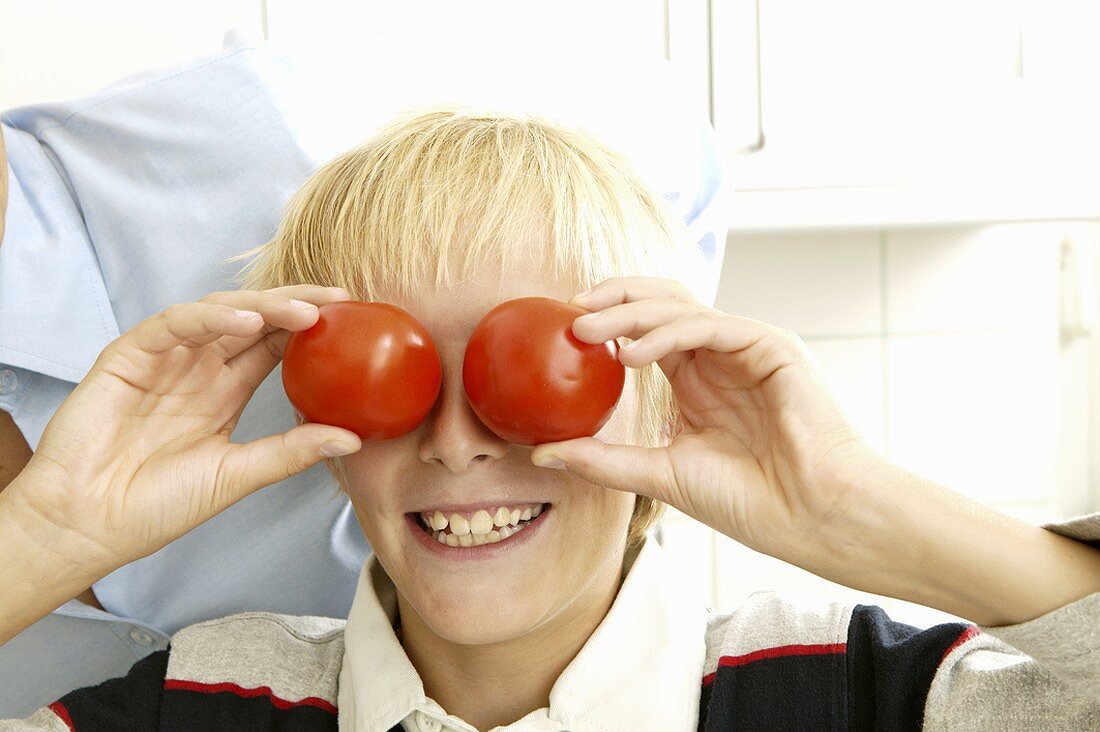 Blonder Junge hält zwei Tomaten vor die Augen