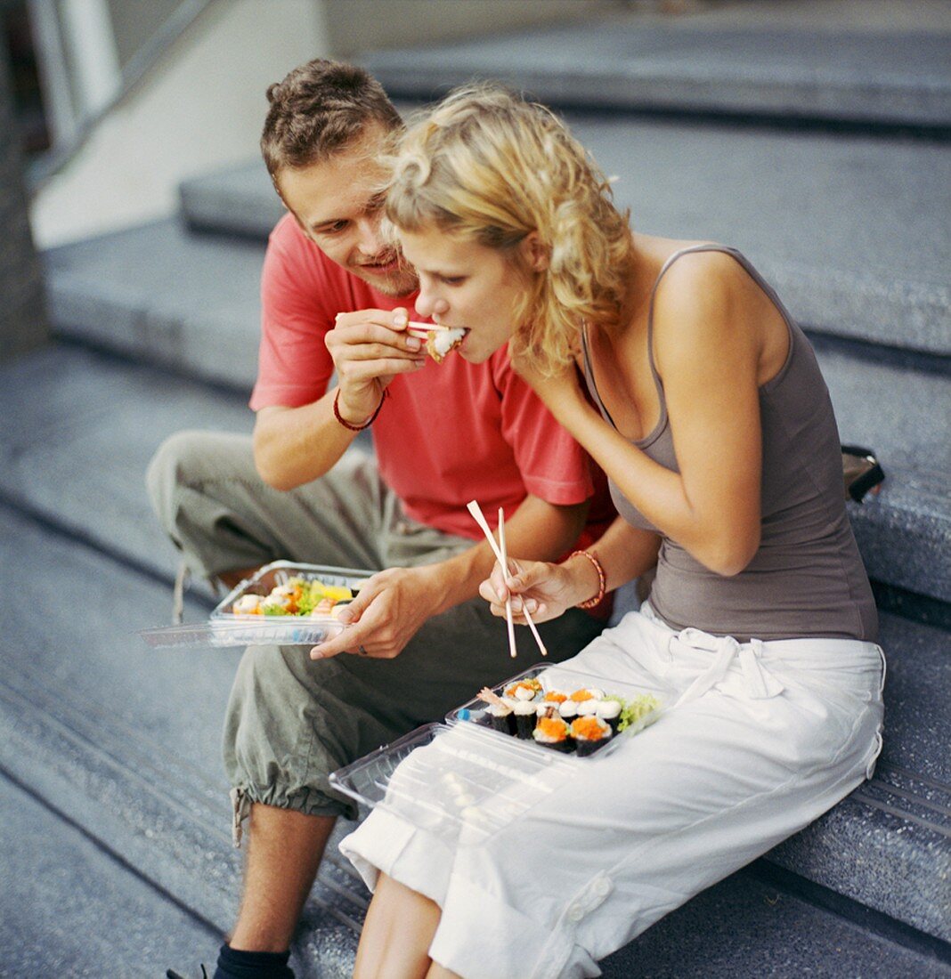 Young couple sitting on steps eating sushi