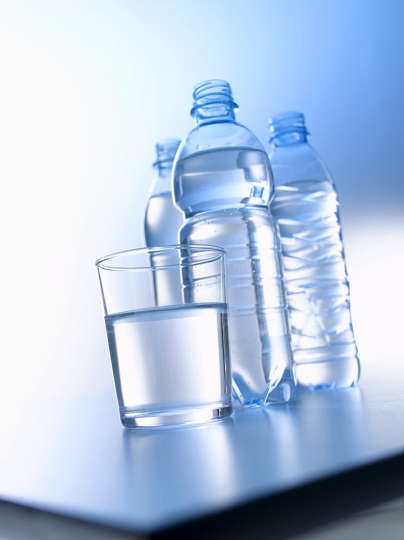 Wasserglas und drei Wasserflaschen auf einem Tisch