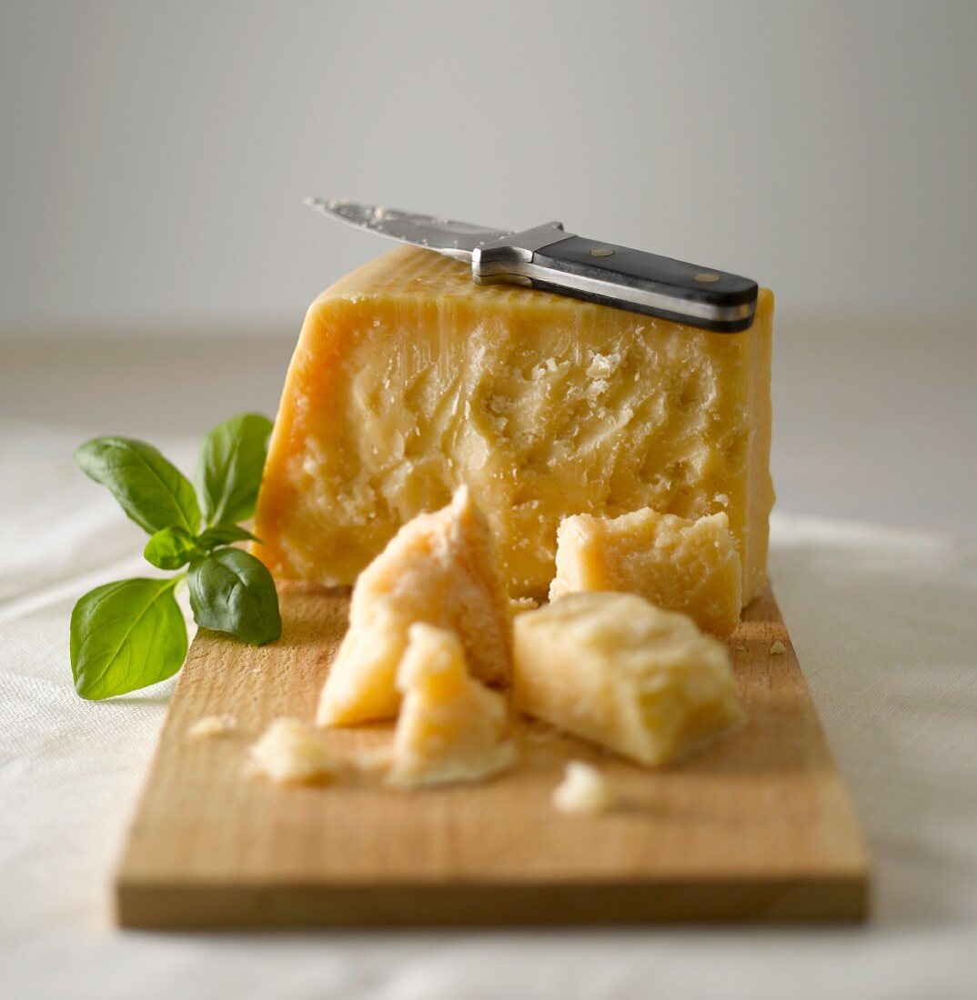 Parmesan mit Messer und Basilikum auf einem Holzbrett