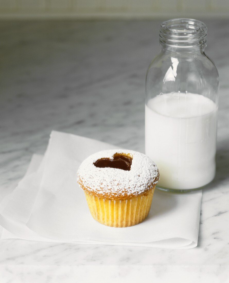 A cupcake with a jam heart and a bottle of milk