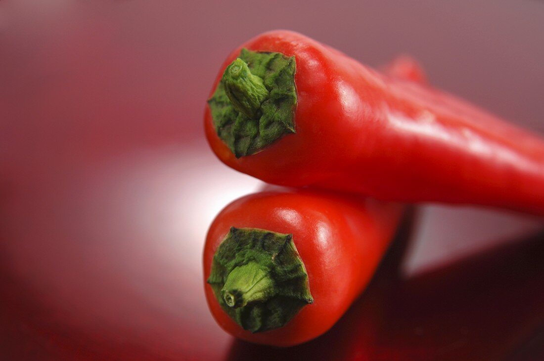 Two red pointed peppers, one lying on top of the other