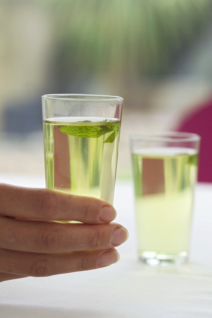 Frau hält ein Glas Grünen Tee mit Minze